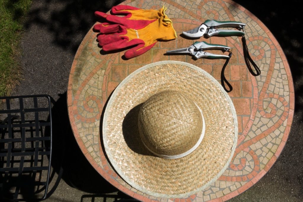 Slaměný klobouk, zahradnické rukavice a nůžky na stole s mozaikou 